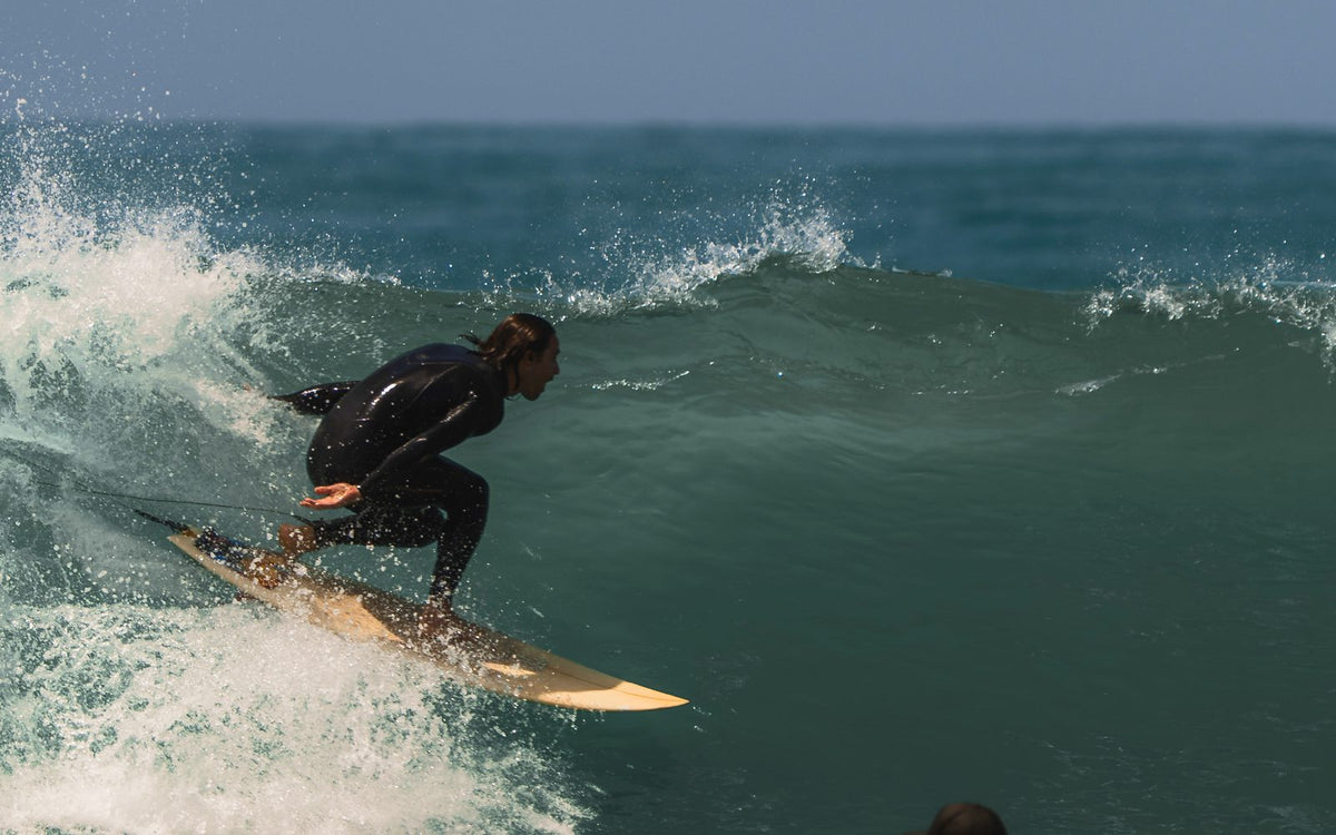 Surfer in a full wetsuit mid-turn on a green wave, spray breaking off the lip behind
