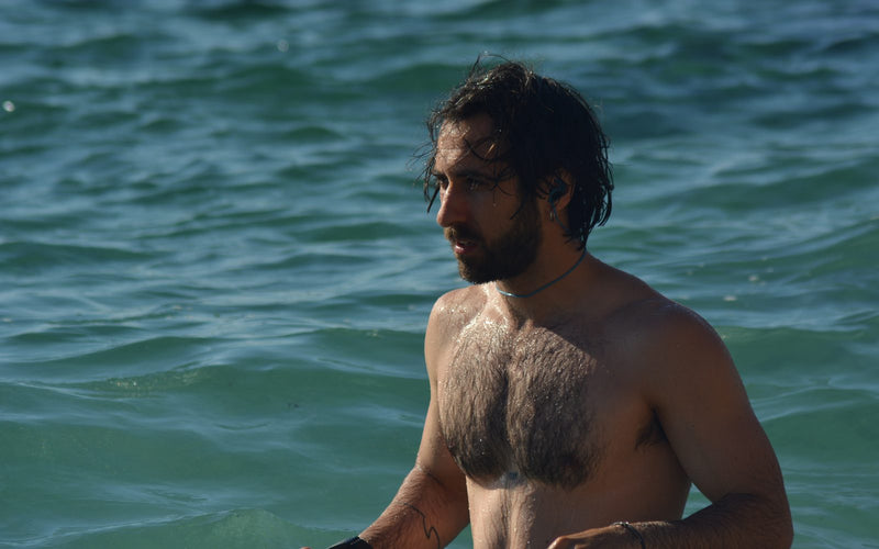 Swimmer standing chest-deep in the sea wearing a SEAR filtered earplug, retention leash around the neck
