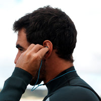 Surfer in a wetsuit inserting a blue SEAR Plug, with the leash routed behind the ear and around the neck