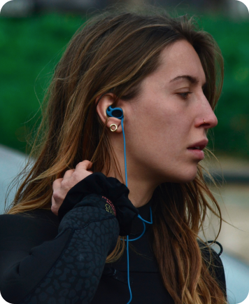 Woman wearing blue water-sports earplugs adjusting her wetsuit collar outdoors.