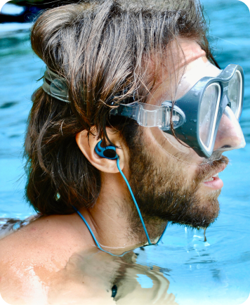 Man wearing swim goggles and blue earplugs floating in water.