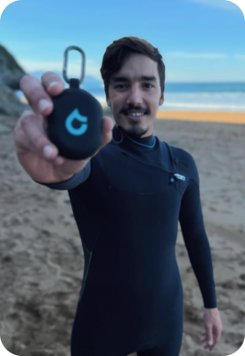 Man holding a black SEAR earplug case toward the camera on the beach.