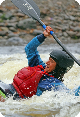 Kayaker paddling through whitewater rapids wearing a helmet and buoyancy vest.