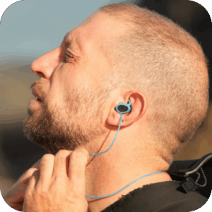 Man adjusting a blue water-sports earplug behind his ear, shown in close-up profile outdoors.