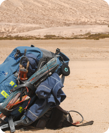 Backpack loaded with kite and water-sports gear resting on sandy ground.