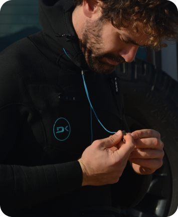 Person in a wetsuit attaching a blue earplug leash in close-up.